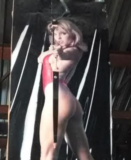 Female model in high heels and red bathing suit shooting recurve bow. Hung from ceiling.